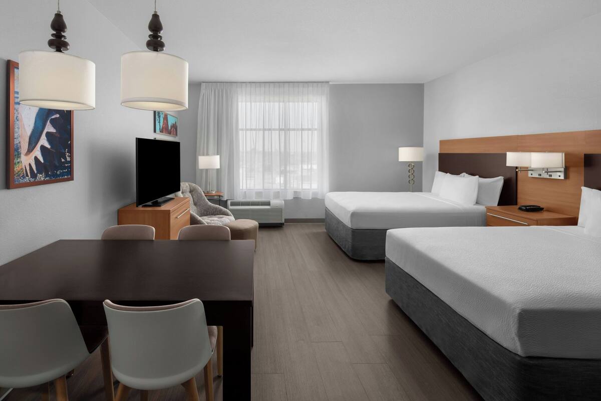 Ett hotellrum med en säng, ett skrivbord med en stol, en tv och ett fönster med gardiner.