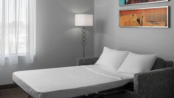 Cama de casal com colchão branco num quarto com parede cinzenta, abajur e duas molduras.