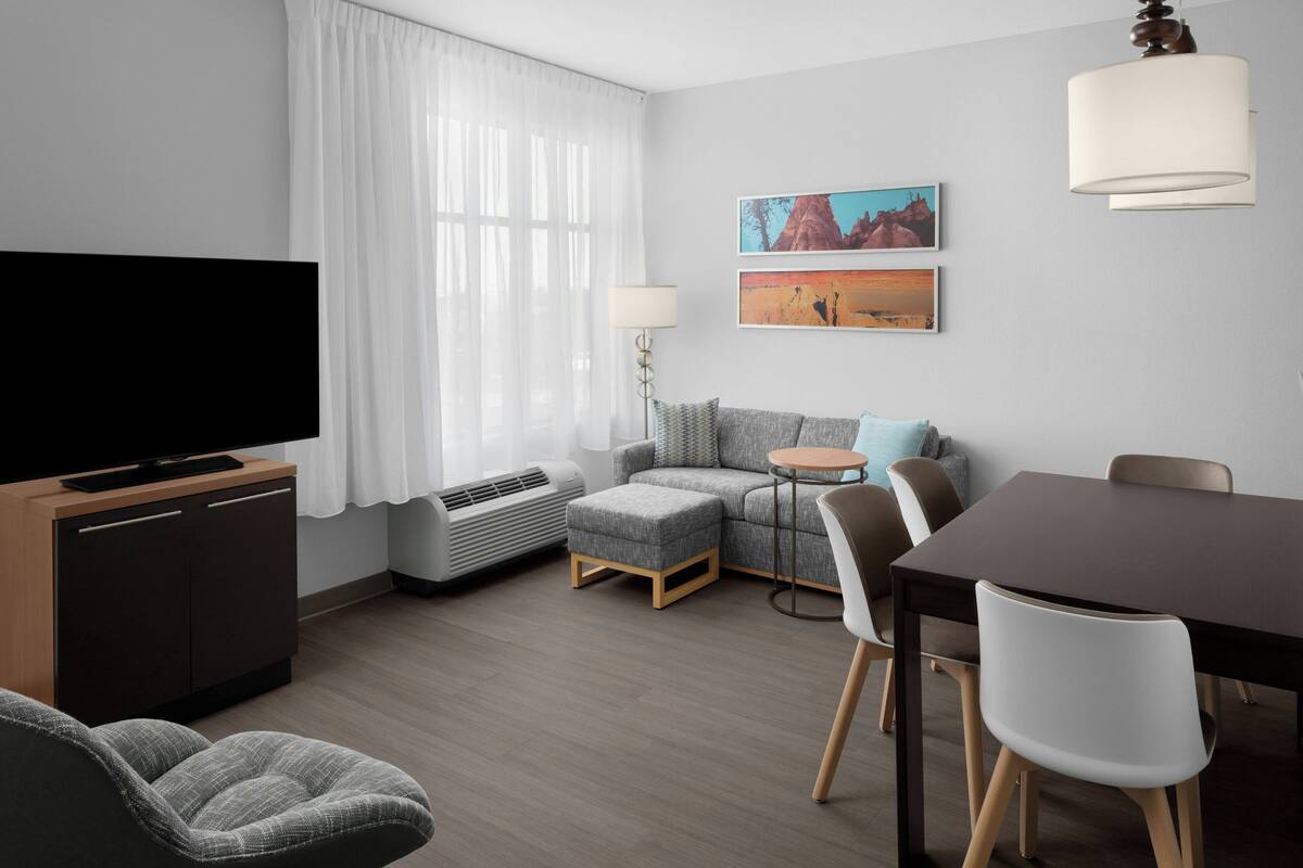 Ett modernt vardagsrum med en platt-TV, en soffa, ett matbord och en lampa.