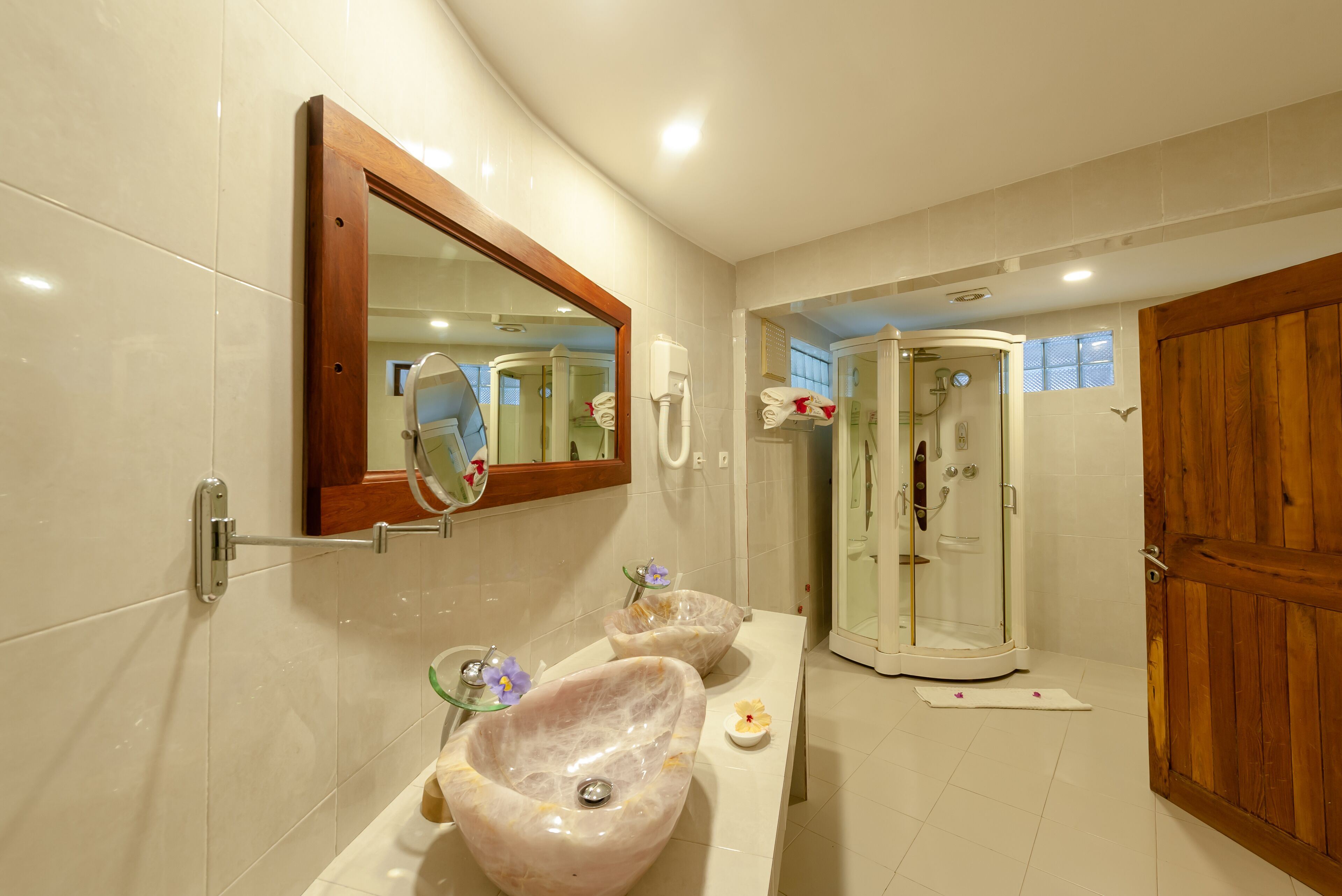 Un baño con dos lavamanos de mármol, una puerta de madera y una cabina de ducha con mampara de vidrio.