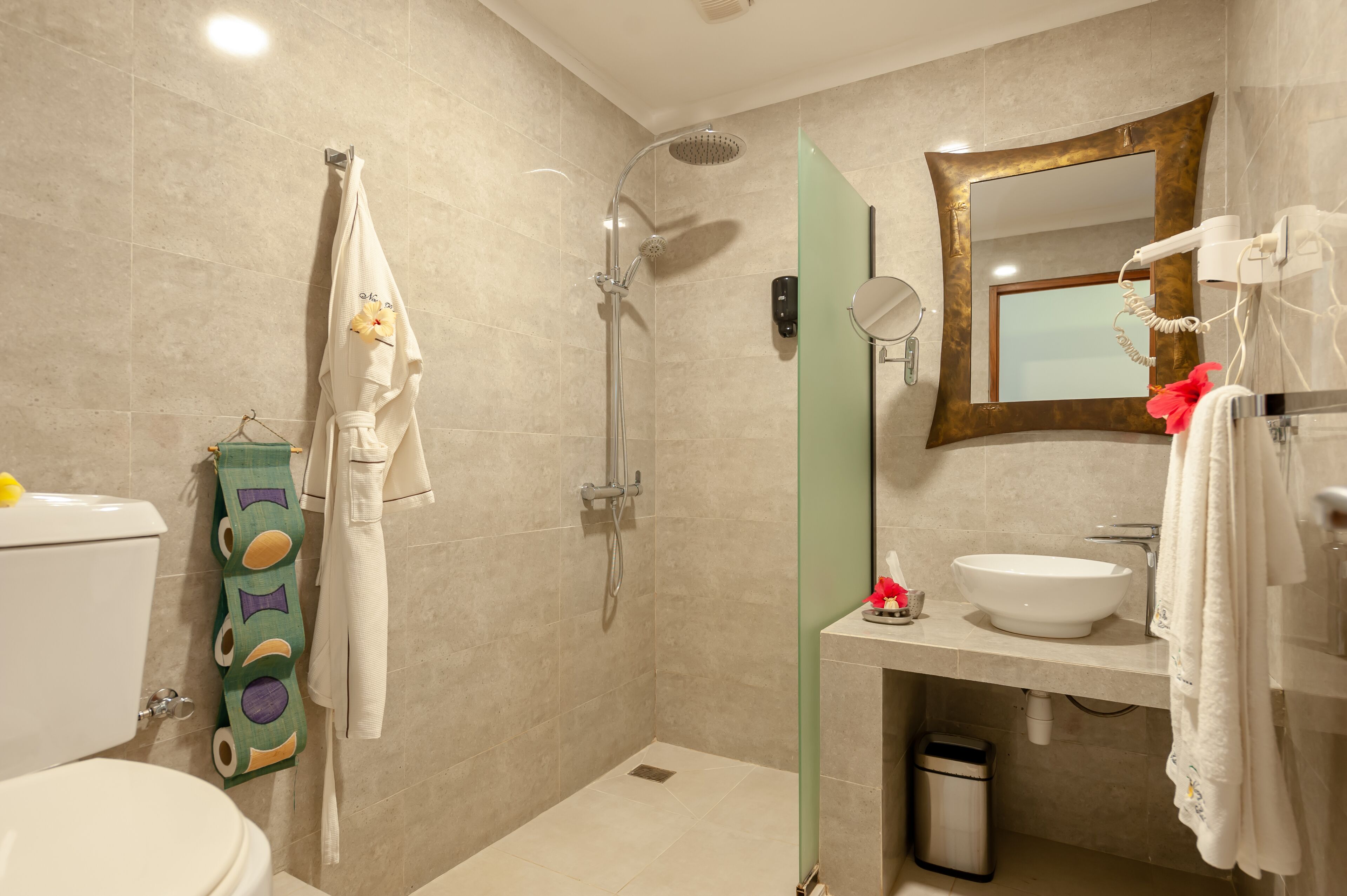 Un baño moderno con ducha, inodoro, lavamanos y un espejo con marco dorado.