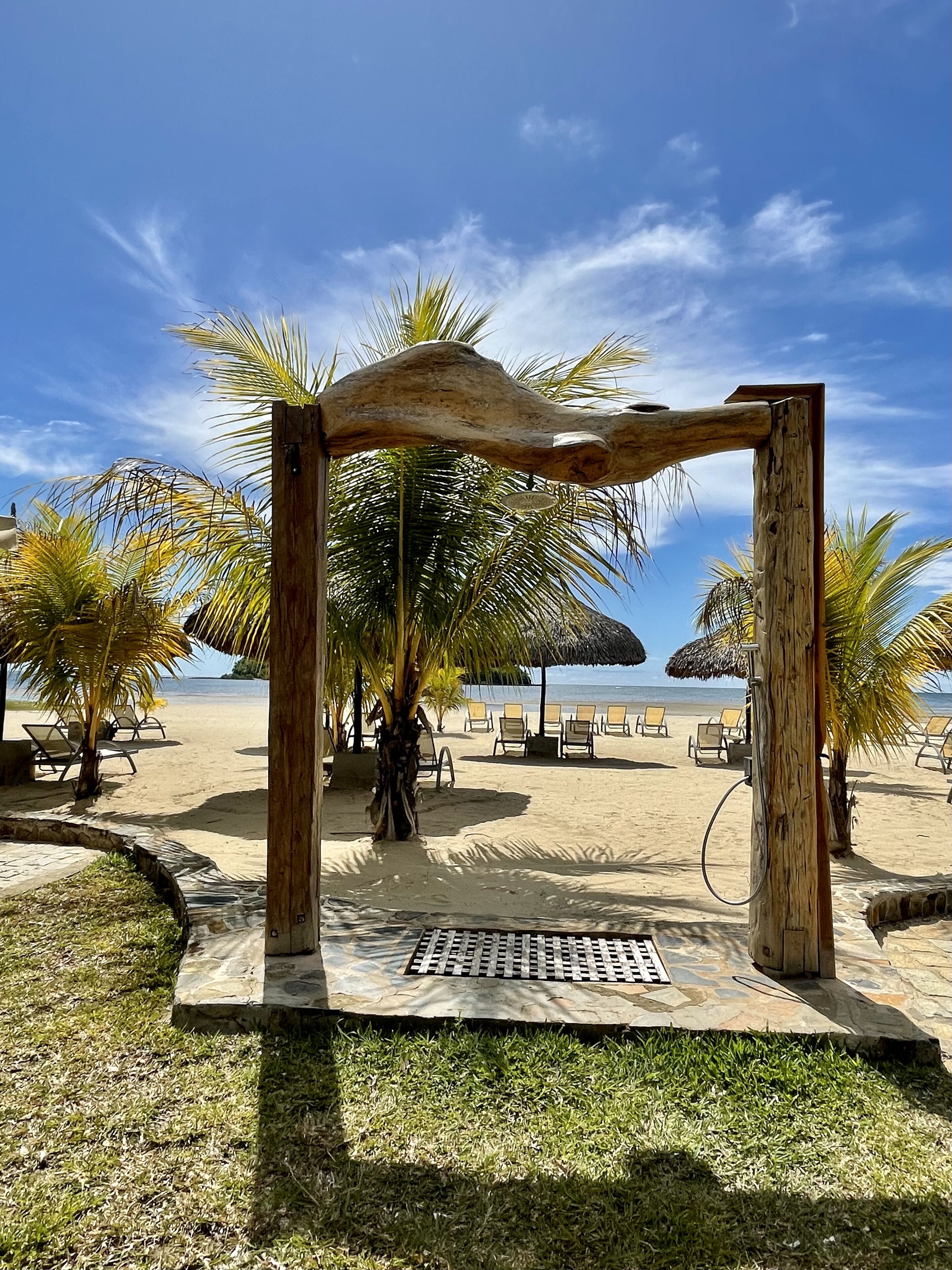 Une plage avec une structure en bois, des palmiers et des chaises longues.