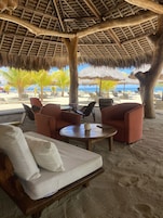 A beachside lounge with a thatched roof, cushioned seating, and a view of the ocean.