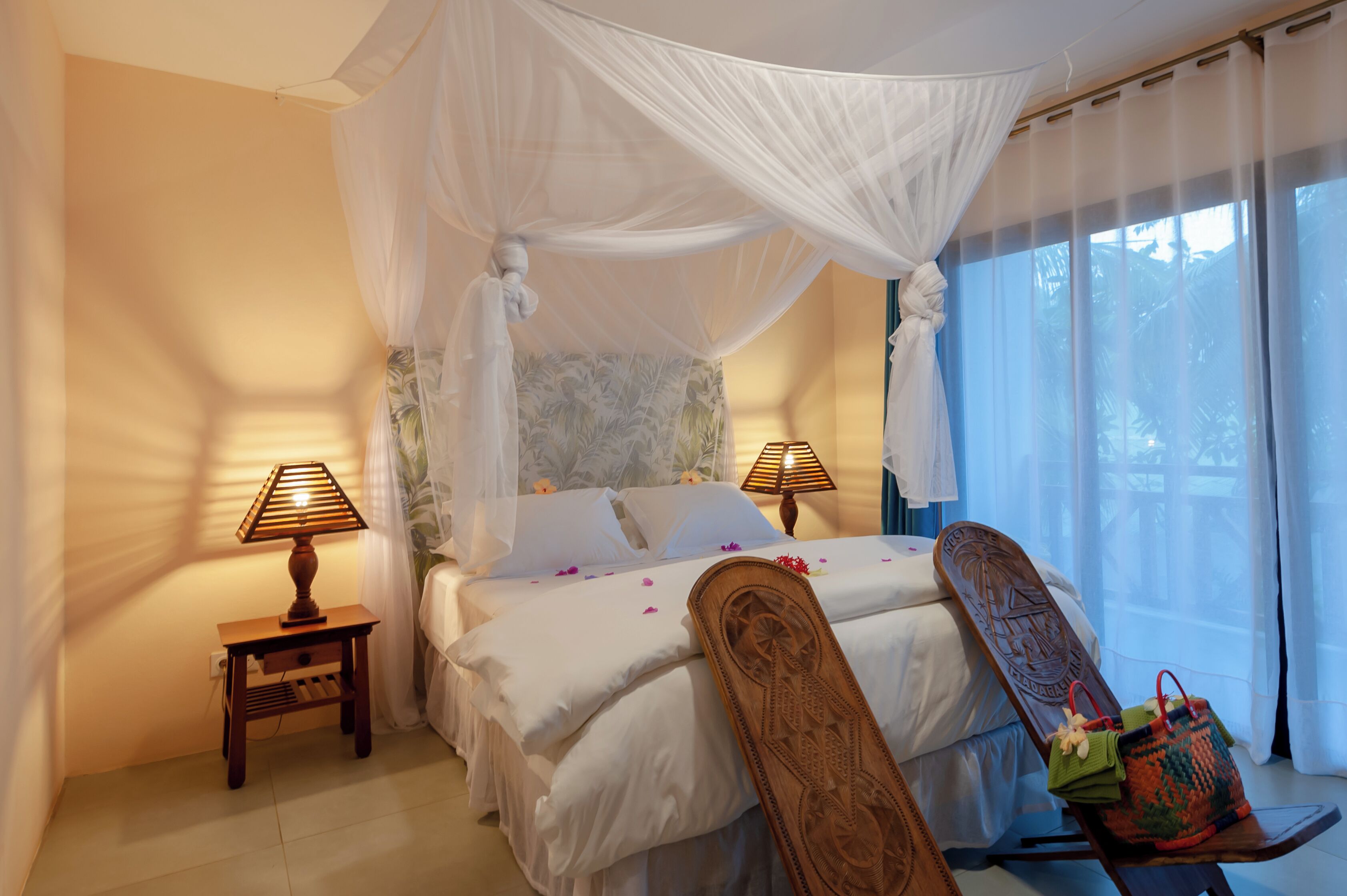 Une chambre à coucher avec un lit à baldaquin, deux lampes de chevet, une chaise en bois et une fenêtre avec des rideaux.