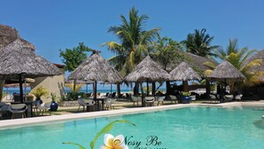 A poolside area with thatched umbrellas, lounge chairs, and a clear view of the ocean. - Nosy Be Hotel & Spa (Nosy Be)