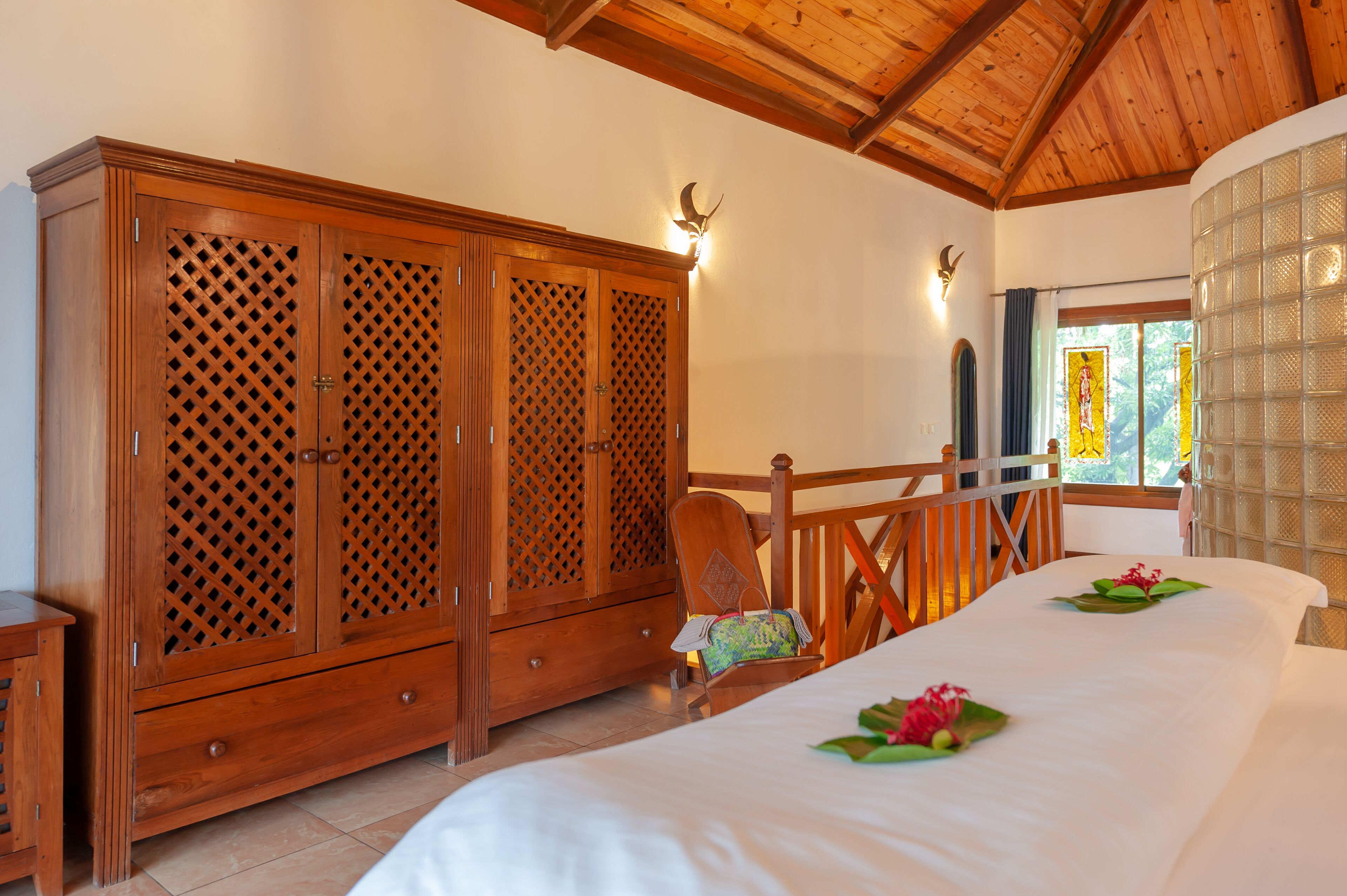 Une chambre avec une armoire en bois, un lit recouvert de draps blancs et une fenêtre donnant sur un paysage verdoyant.