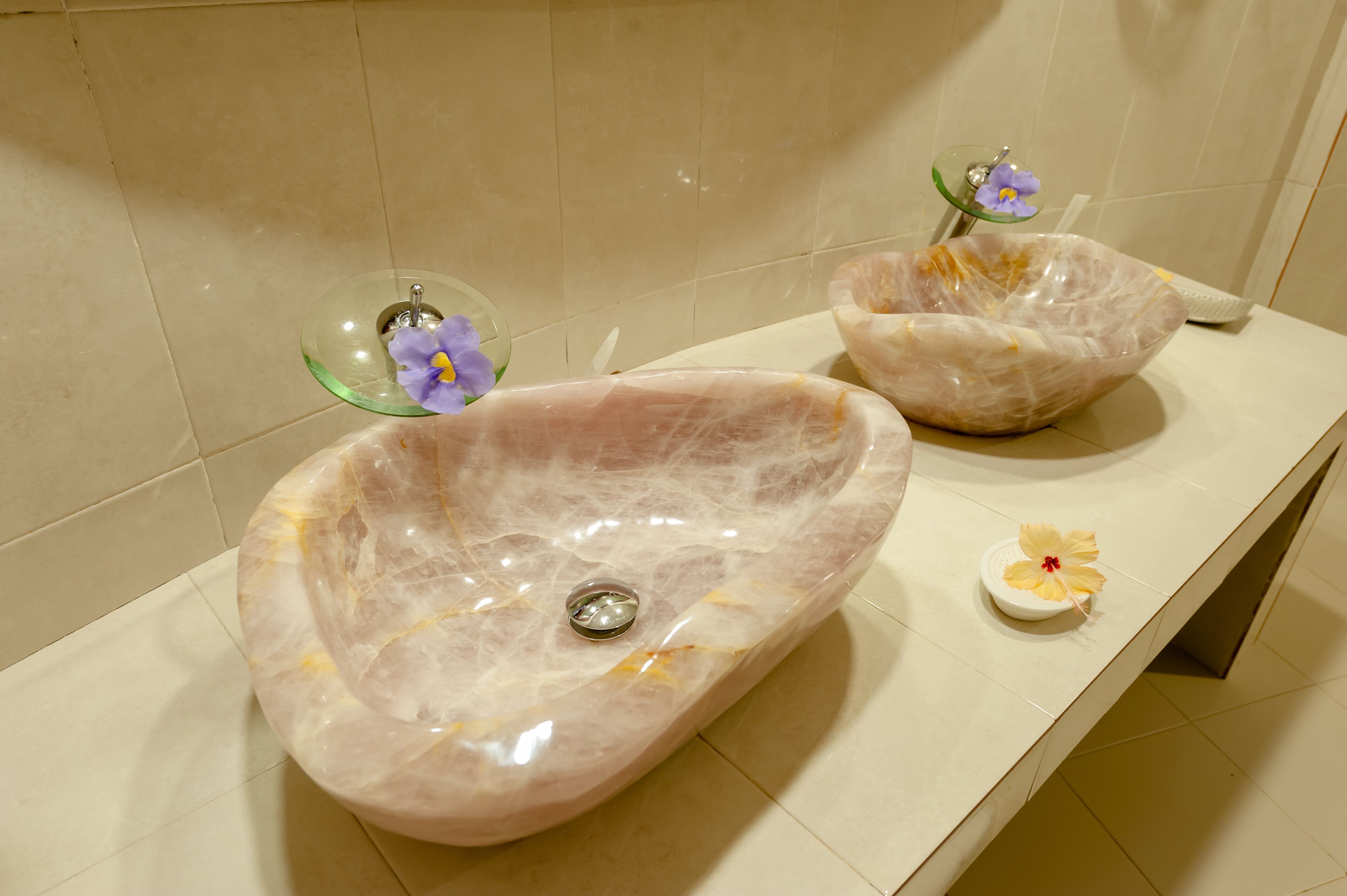 A bathroom with two oval marble sinks and a small decorative bowl with a flower.