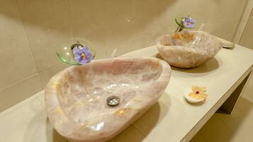 A bathroom with two oval marble sinks and a small decorative bowl with a flower.