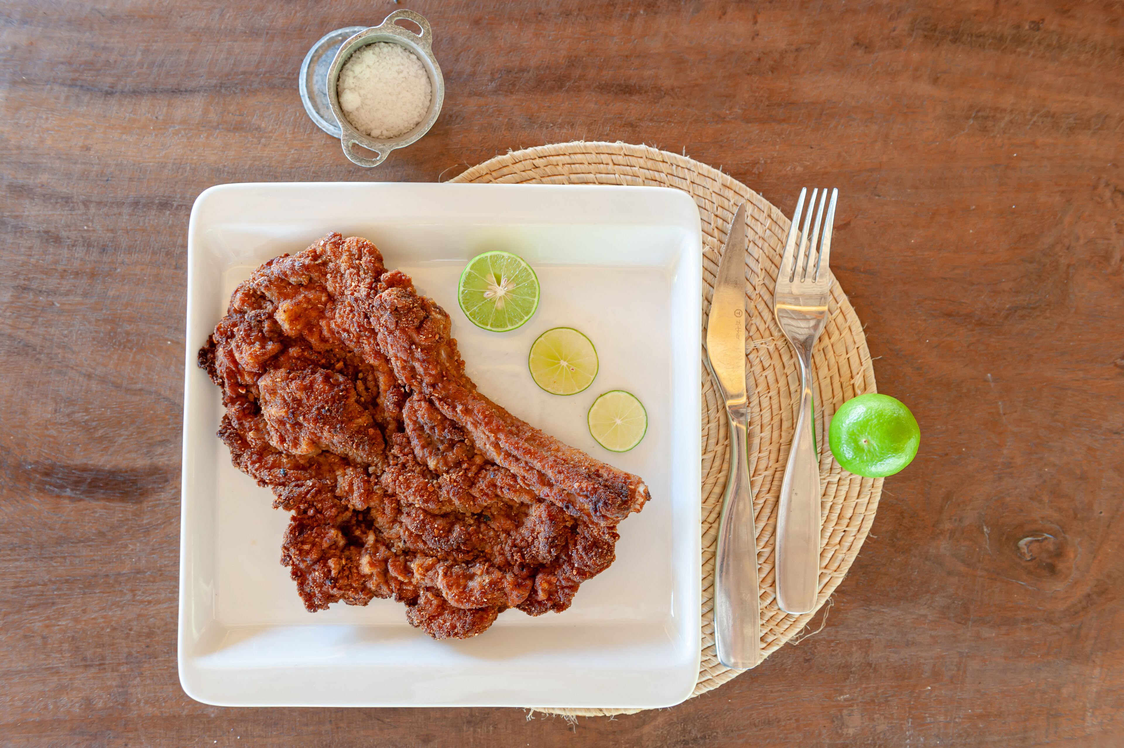 A plate of fried fish with lime wedges on a wooden table.