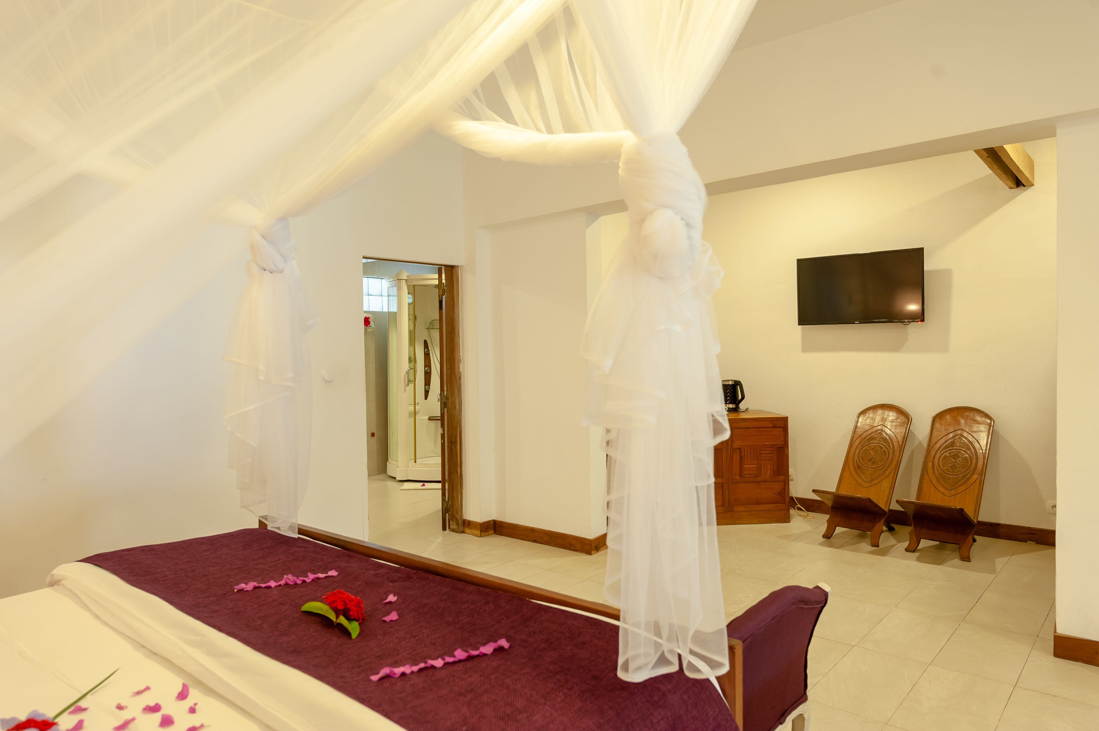 A bedroom with a canopy bed, a television on the wall, and a wooden cabinet.