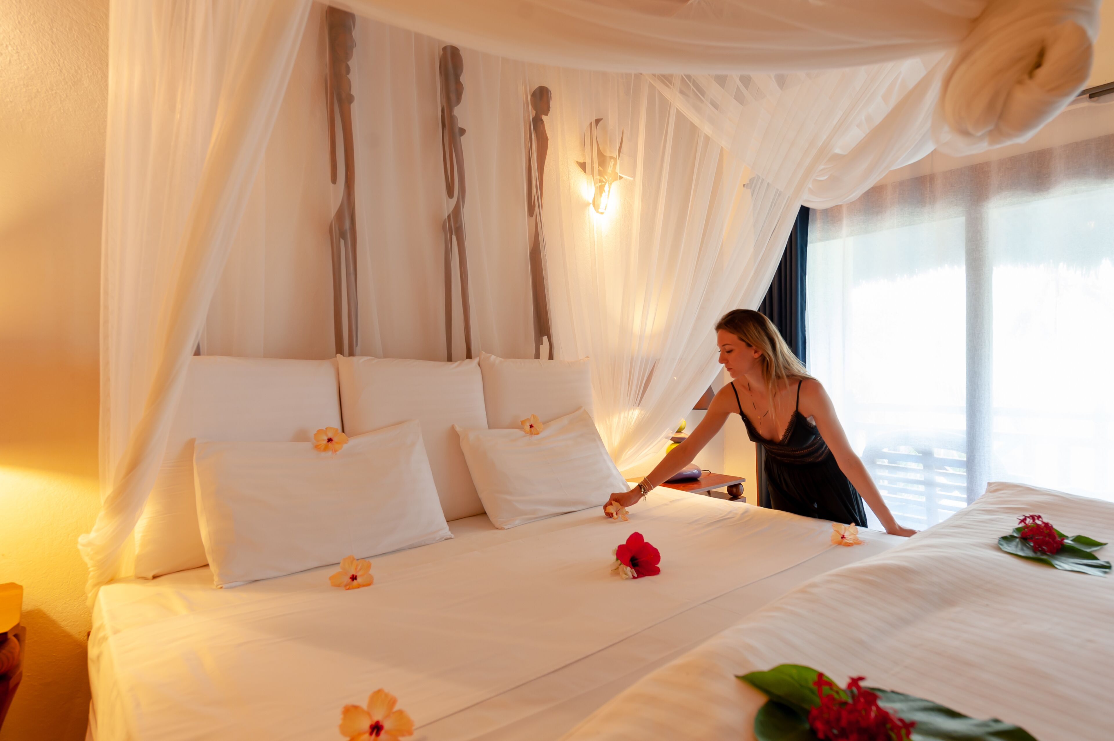 A bed with white linens and floral decorations, a canopy, and a wall-mounted light fixture.