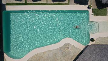 Una vista aerea di una piscina con acqua cristallina, circondata da un solarium piastrellato e aree verdi.