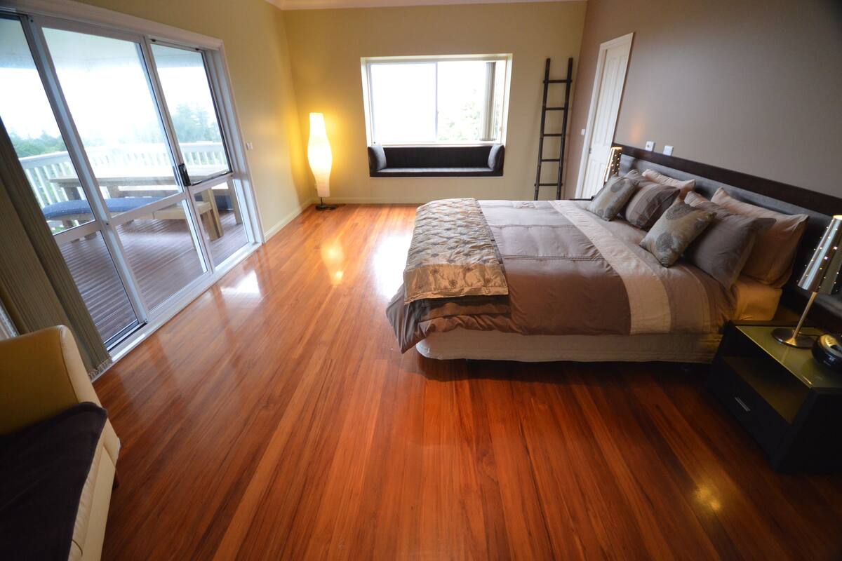 A bedroom with a large bed, a window seat, and a view of a balcony.
