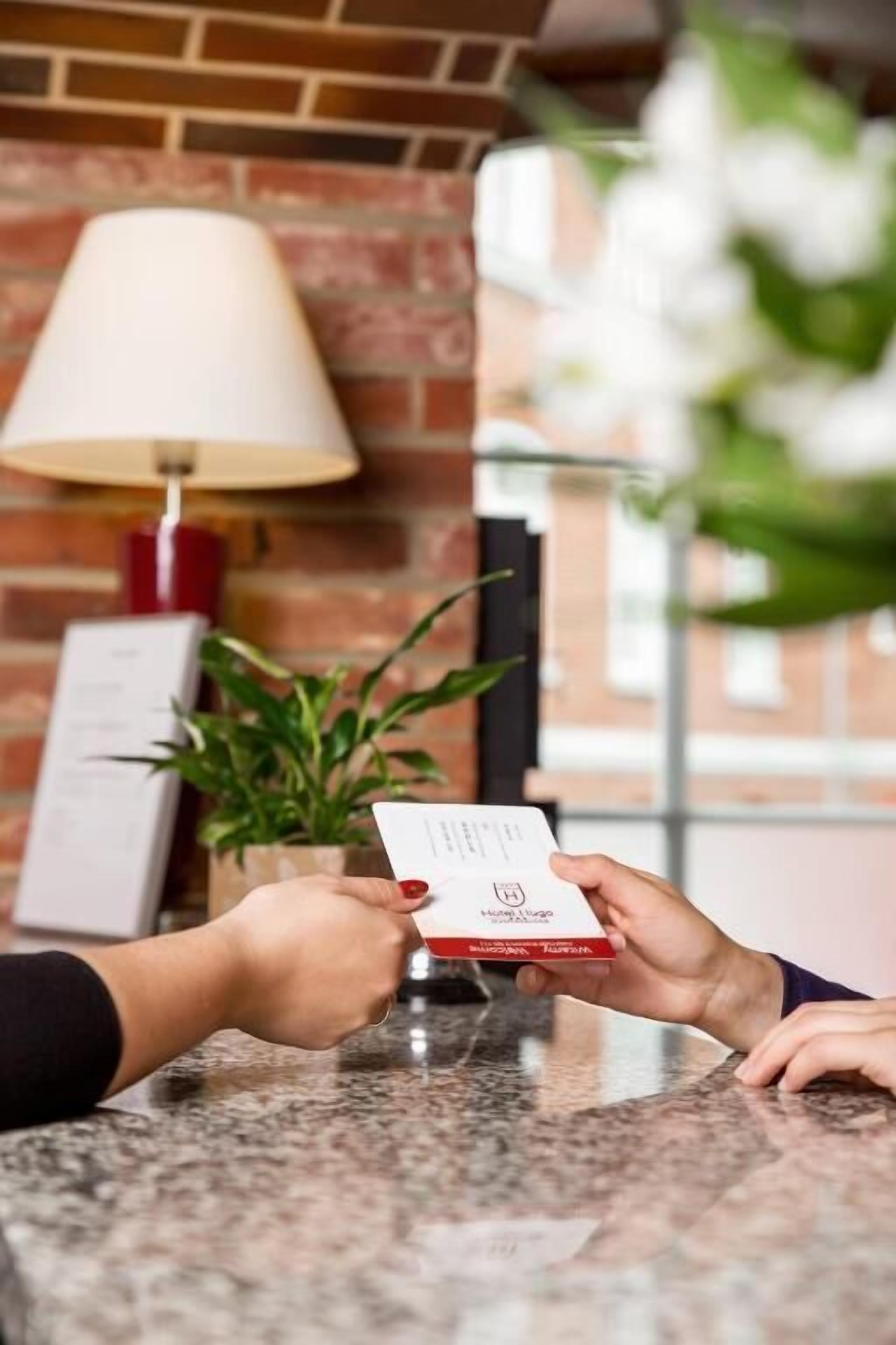 Una persona sosteniendo una tarjeta en la recepción, con una lámpara y una planta de fondo.