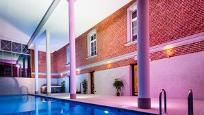 Une piscine intérieure avec un mur en briques et des colonnes, entourée de plantes en pot.
