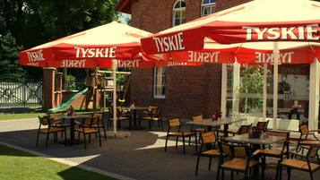 Outdoor seating with red umbrellas and a brick building in the background.