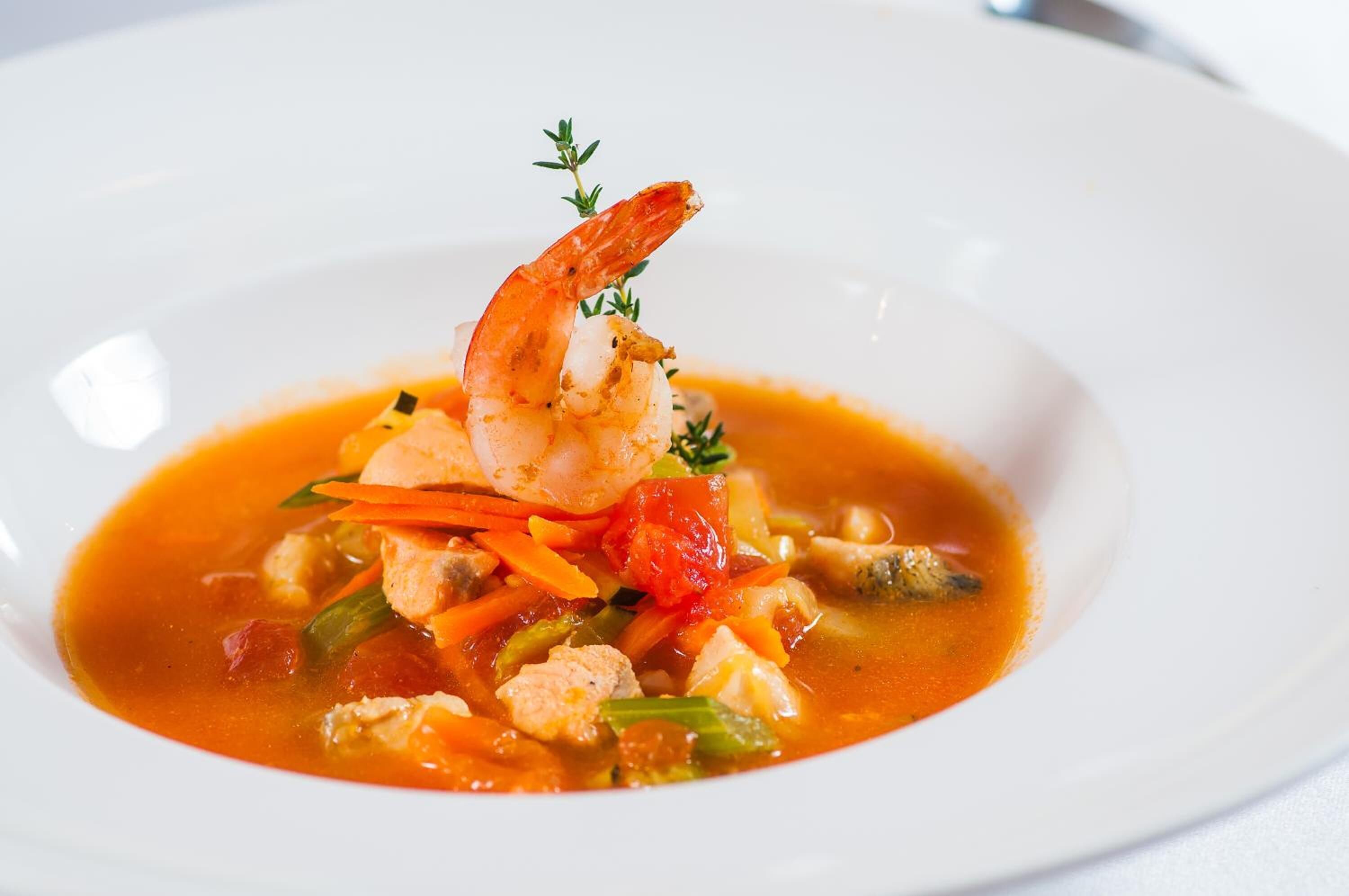 Prato de frutos do mar com camarão, cenouras e tomates em um prato branco.