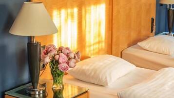 A hotel room with a bed, a bedside table with a lamp, and a vase of flowers.
