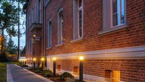 Un bâtiment en briques avec un trottoir dallé et des bornes lumineuses.