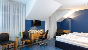 A hotel room with a bed, desk, chairs, a TV, and a lamp.