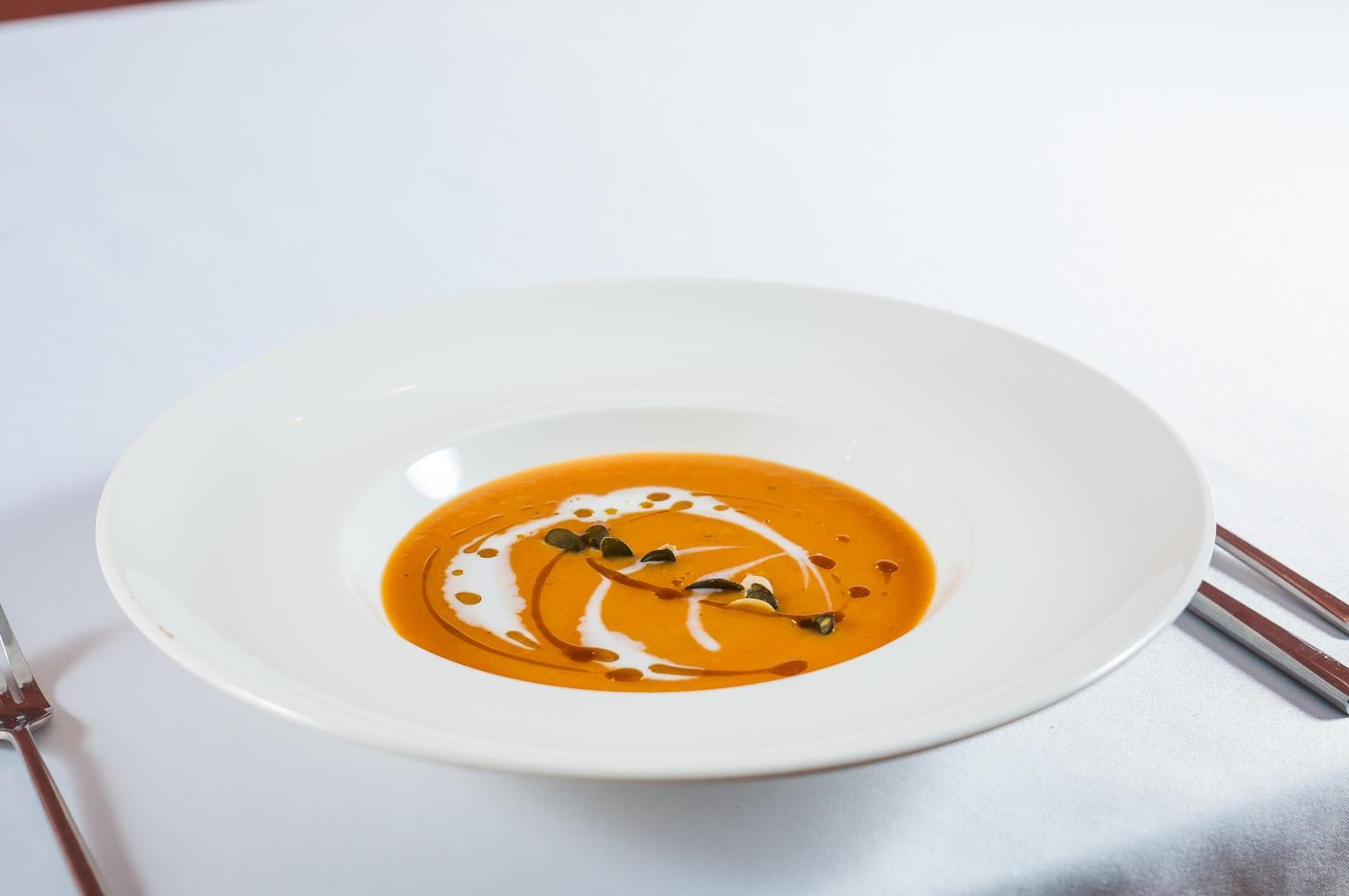 Un plato blanco con sopa y un hilo de crema, acompañado de un tenedor.