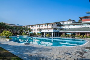 Ein Swimmingpool mit umlaufender Terrasse, ein mehrstöckiges Gebäude und ein klarer, blauer Himmel.