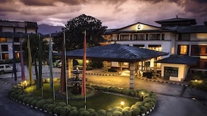 A hotel with a traditional architectural style, featuring a central courtyard with a fountain, surrounded by neatly trimmed bushes and a variety of flags. - Hotel Annapurna (Kathmandu)