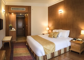 Ein Hotelzimmer mit einem großen Bett, Nachttischlampen, einem Nachttisch, einem Schreibtisch und einer Wandpaneele aus Holz.