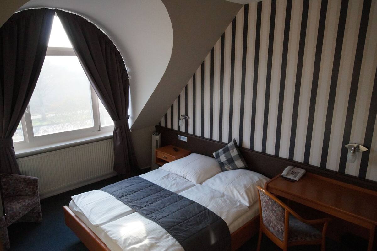 Habitació d'hotel amb un llit, una taula de nit, una cadira, una finestra amb cortines i una paret amb dibuixos de ratlles.