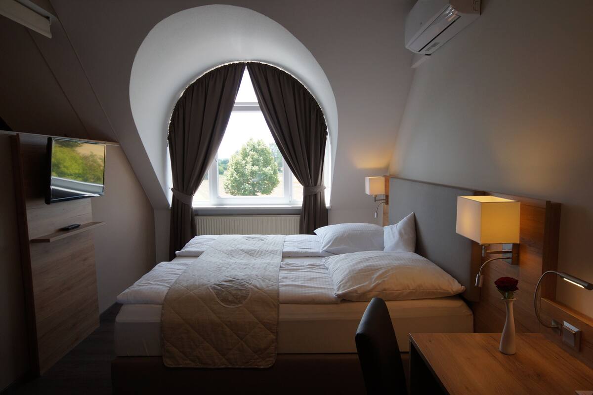 Habitació d'hotel amb llit, televisió, escriptori i finestra amb cortines.