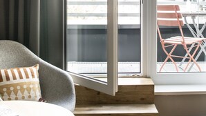 A modern room with a grey chair, a small round table, and a window with a view of a building labeled "BOLD". - Bold Hotel München Giesing (Munich)