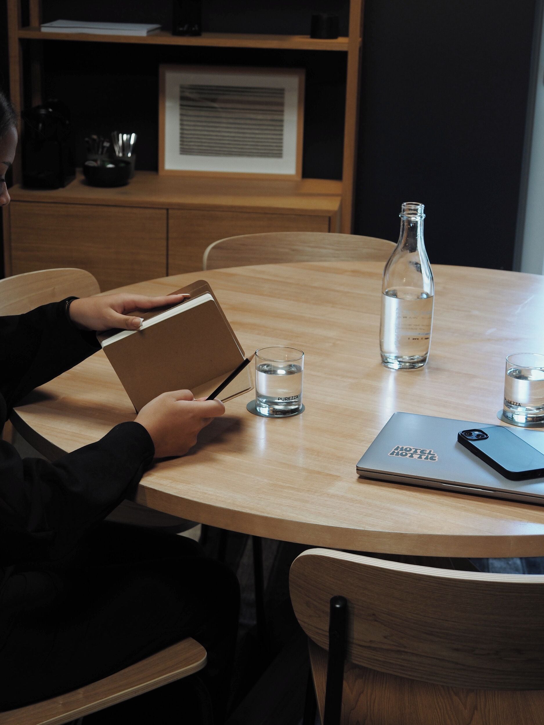 A person at a wooden table with a notebook, a smartphone, and two glasses of water.