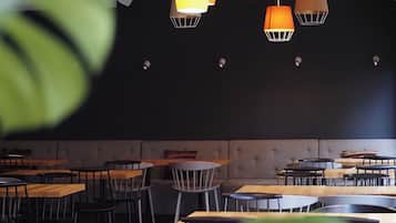 A restaurant with multiple tables and chairs, hanging pendant lights, and a dark ceiling.