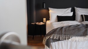 A bedroom with a bed, a bedside table, a lamp, and a wall-mounted light fixture. - Bold Hotel München Giesing (Munich)
