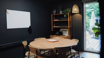 Un salón de conferencias con una mesa redonda de madera, seis sillas, una pizarra, una estantería con plantas y un ventanal con vistas al verdor.