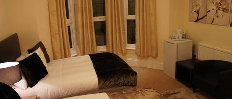 Une chambre à coucher comprenant un lit, une table de chevet, une lampe, une chaise, un radiateur et une fenêtre avec des rideaux.