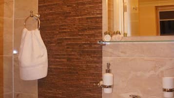 A bathroom with a marble wall, a white sink, and a towel hanging on a metal rack.