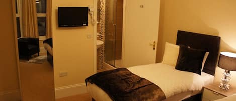 Een hotelkamer met een bed, nachtkastje met lamp, spiegel, televisie en een badkamer met douche.