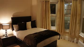 Un dormitorio con cama, mesita de noche, lámpara y cortinas.