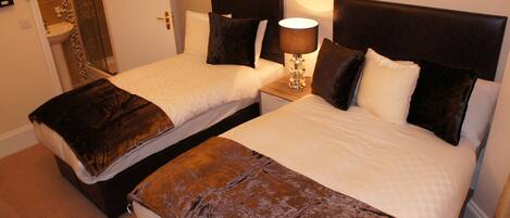 Two single beds with dark headboards and white bedding, a bedside lamp, and a small bedside table.