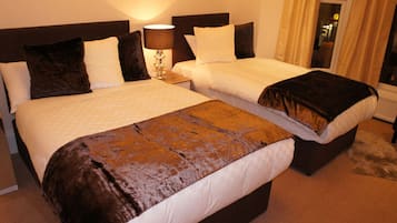 A hotel room with two beds, a nightstand with a lamp, and a window with curtains.