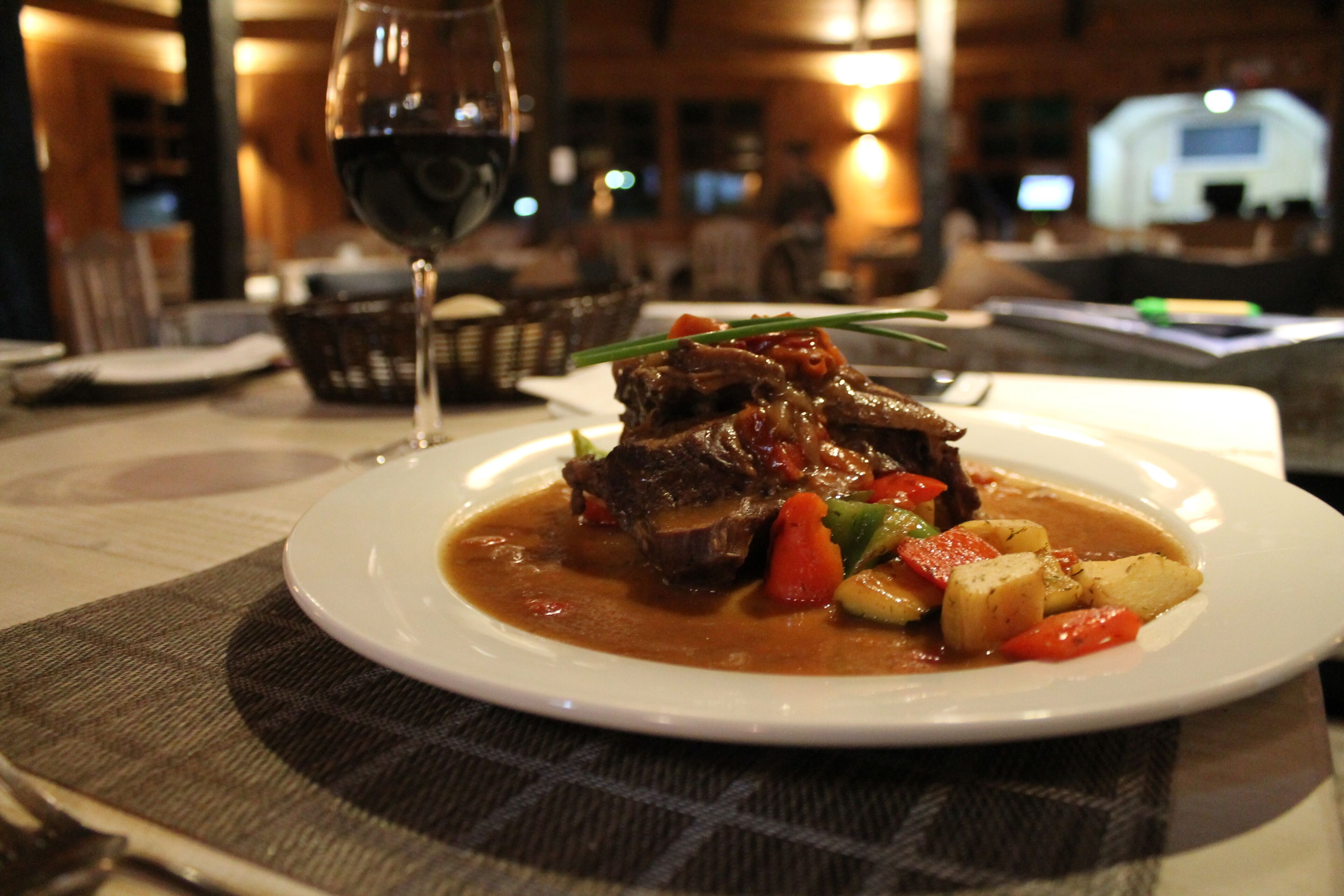 Ein Teller Rindereintopf mit Gemüse und ein Glas Rotwein auf einem Tisch.