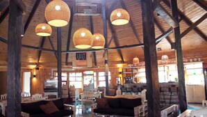 A rustic interior with wooden beams, a dining area with white chairs, and a kitchen in the background. - Termas de Aguas Calientes (Puyehue)