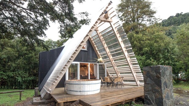 A wooden structure with a slanted roof, a circular water tank, and a seating area with tables and chairs. - Termas de Aguas Calientes (Puyehue)