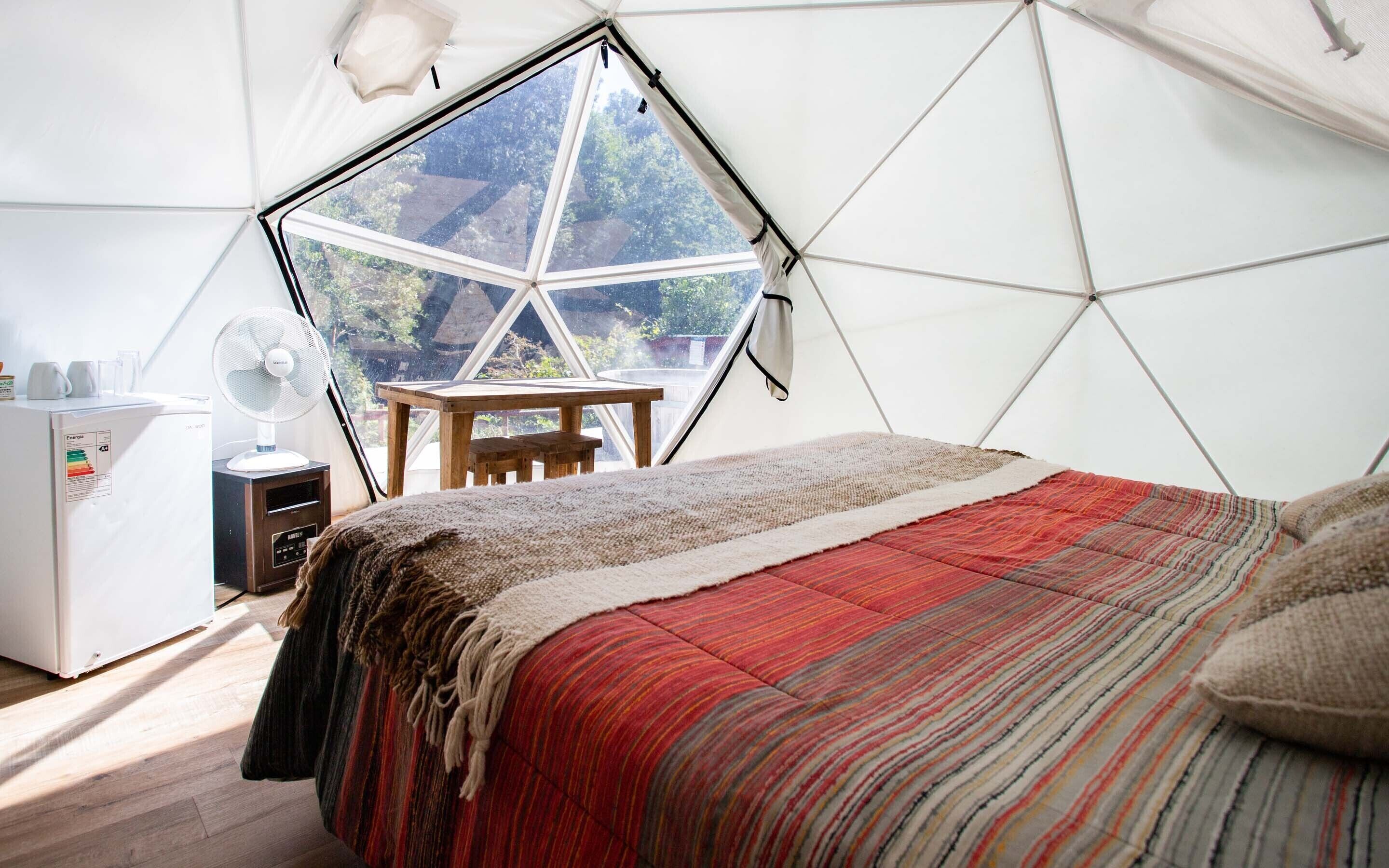 A room with a geometric window, a bed with a striped blanket, a small table, and a fan.