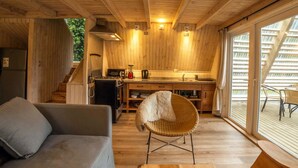 A cozy cabin interior with a wooden interior, a kitchenette, a dining area, and a large window. - Termas de Aguas Calientes (Puyehue)