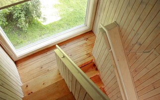 Una escalera de madera con un ventanal en la parte superior, que desciende a un nivel inferior.