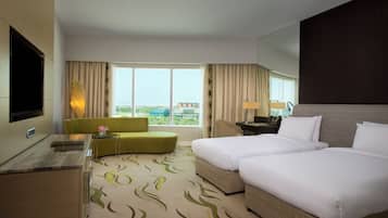 Quarto de hotel com duas camas, um sofá, uma televisão, uma mesa de trabalho e uma janela com vista.