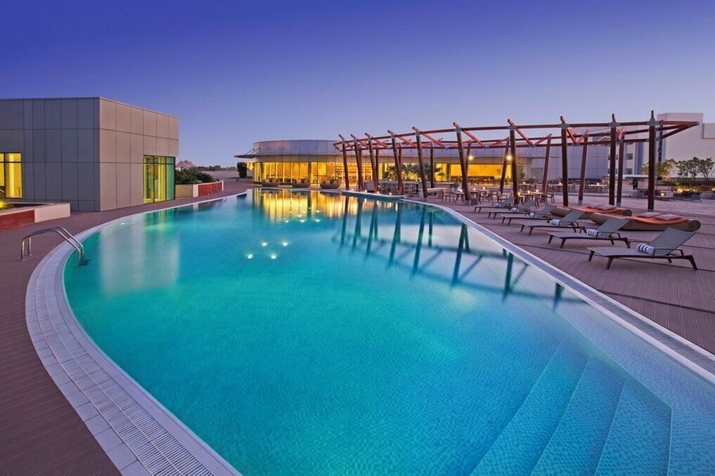 A swimming pool with lounge chairs and a covered seating area, surrounded by modern buildings.