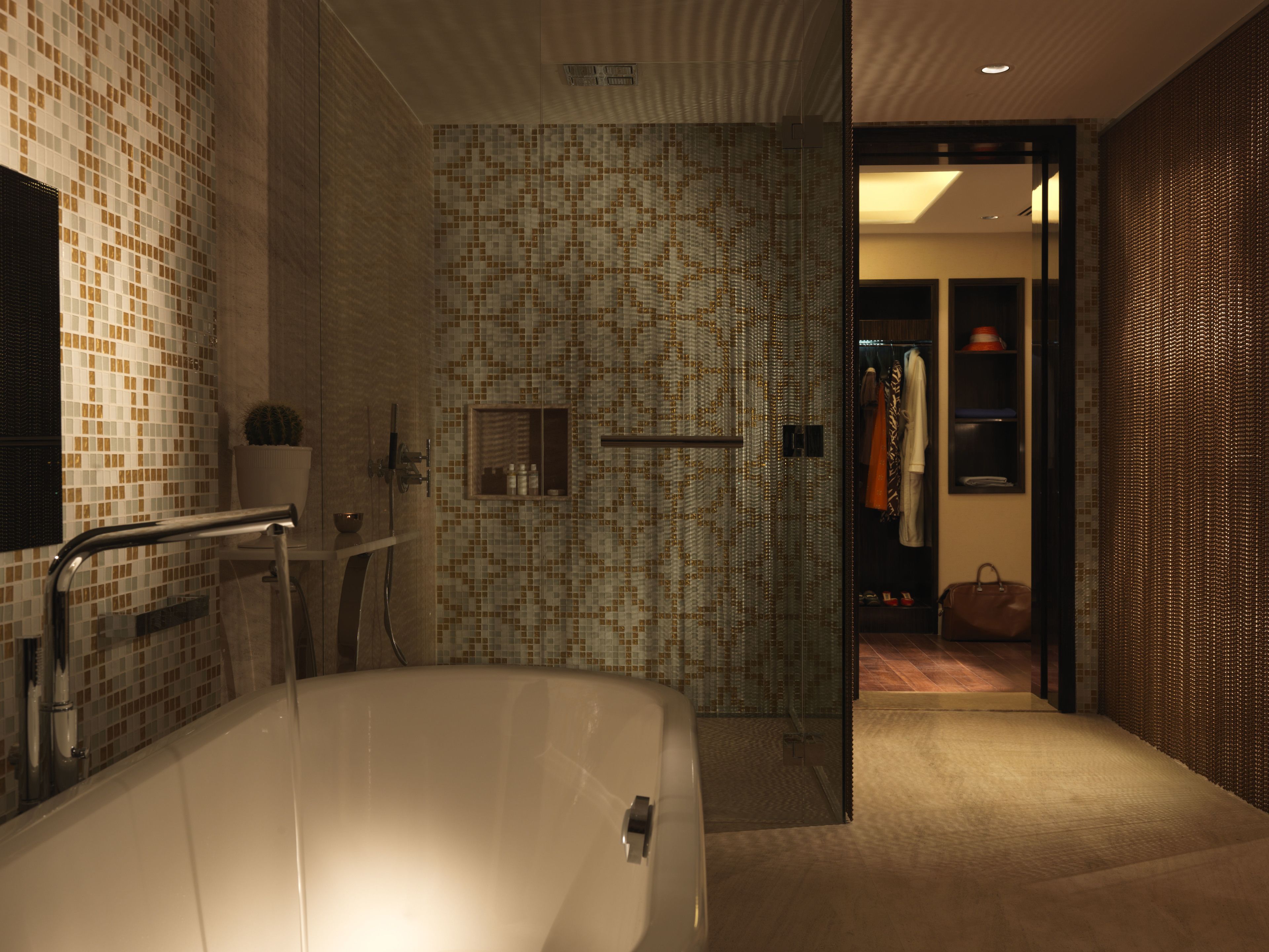 A modern bathroom with a freestanding bathtub, a shower area with mosaic tiles, and a walk-in closet with hanging clothes.